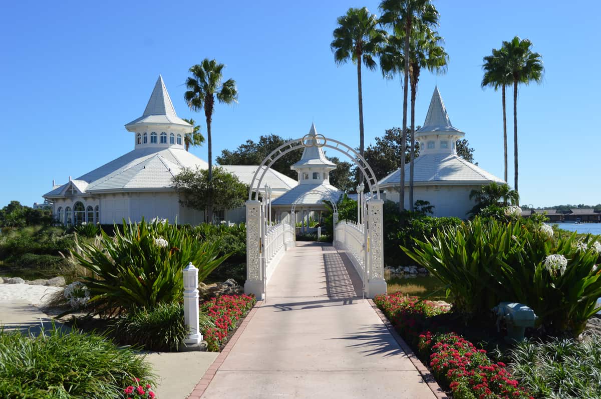 Disney's picturesque white wedding chapel with iconic turrets, palm trees, and lush walkway under a sunny Walt Disney World sky.