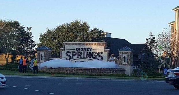 Bubbles overflow the Disney Springs entrance sign in a playful Walt Disney World stunt, with Cast Members in vests nearby.