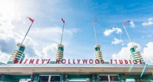 Disney’s Hollywood Studios entrance sign with art deco towers, red flags, and blue sky—your adventure begins here!.