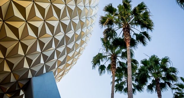 Spaceship Earth at EPCOT rises beside soaring palm trees beneath a cloudless sky, capturing iconic Disney World excitement.