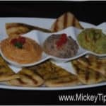 A trio of flavorful dips with pita bread on a white plate, MickeyTips.com watermark—great snack idea for your next Disney trip!.