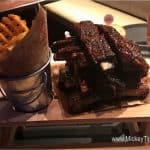 Waffle fries in a metal bucket and saucy glazed ribs served on a wooden board at Planet Hollywood Observatory in Disney World.