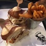 Dig into a Planet Hollywood grilled chicken sandwich on a pretzel bun, with slaw and waffle fries—a Disney World fan favorite!.