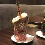 Epic milkshake creation at Planet Hollywood Observatory, Disney World—towering cake, sprinkles, rainbow stick on a wooden table.