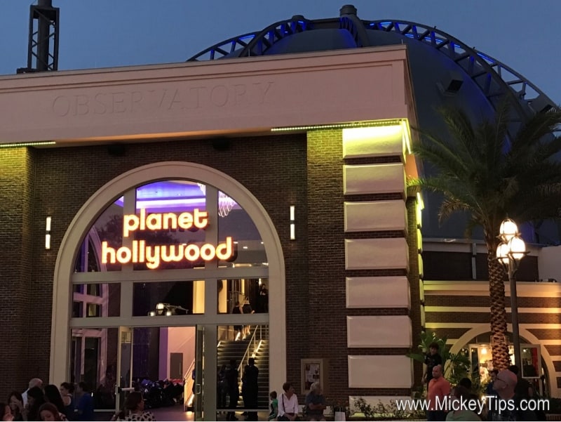 Planet Hollywood Observatory glowing at dusk, neon lights shining as Disney World guests gather outside for a night of fun.