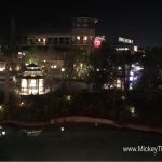Disney Springs waterfront restaurant aglow at night, lights twinkling by Planet Hollywood. www.MickeyTips.com in corner.