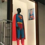 Superman's iconic suit showcased on a mannequin at Planet Hollywood Observatory, with Superman's photo featured in the background.