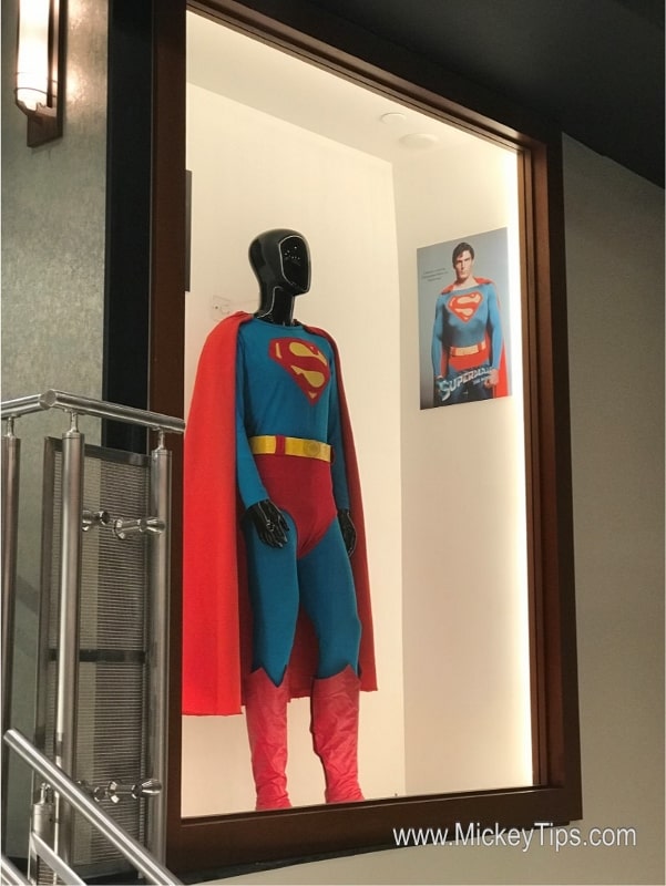 Superman's iconic suit showcased on a mannequin at Planet Hollywood Observatory, with Superman's photo featured in the background.