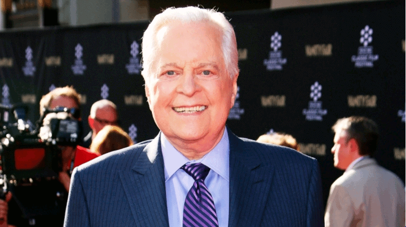 Robert Osborne-style host beaming in a suit on the red carpet, with entertainment fans and press capturing the Hollywood moment.