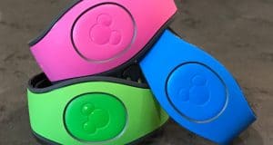 A stack of vibrant Disney World Magic Bands—pink, green, and blue—ready for your next adventure on a gray tabletop.