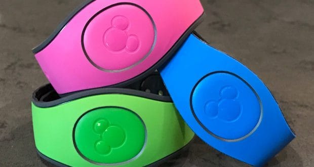 A stack of vibrant Disney World Magic Bands—pink, green, and blue—ready for your next adventure on a gray tabletop.