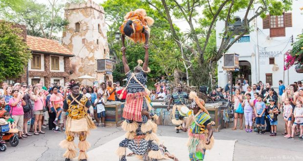 Stilt dancers in vibrant costumes entertain guests amid a lively village scene, embodying the festive magic of Disney World.