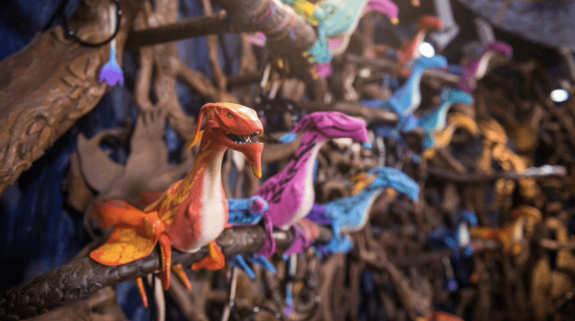 Pandora’s Banshee Connect dragon puppets perch on branches in a shop, with Disney World’s magic blurred in the backdrop.
