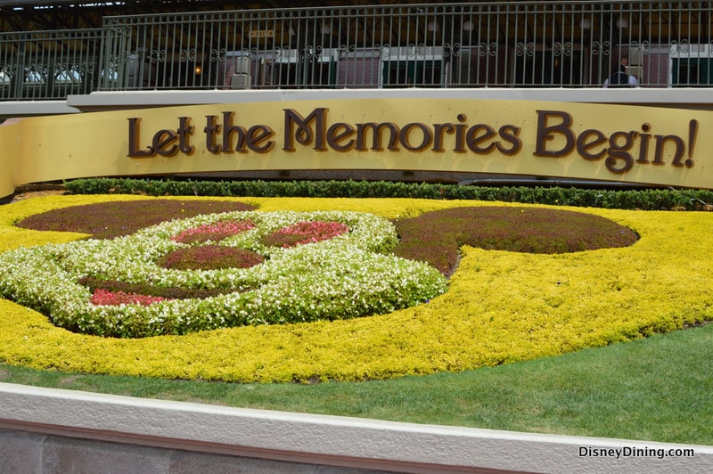 Mickey Mouse-shaped flower bed with a "Let the Memories Begin!" sign welcomes guests to Disney World magic.