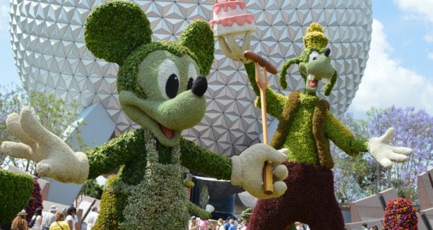 Mickey and Goofy topiaries with a festive cake in front of Epcot’s Spaceship Earth, marking 20 magical years at Disney World.
