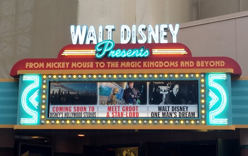 Walt Disney marquee aglow in neon, showcasing posters for new and fan-favorite park attractions with classic Disney characters.
