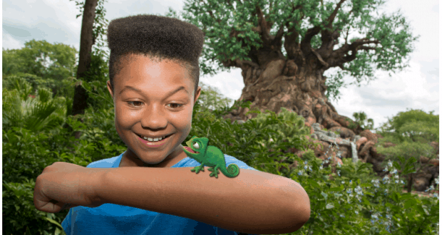 A boy smiles at a cartoon chameleon on his arm with the Tree of Life behind—a whimsical Magic Shot at Disney’s Animal Kingdom.