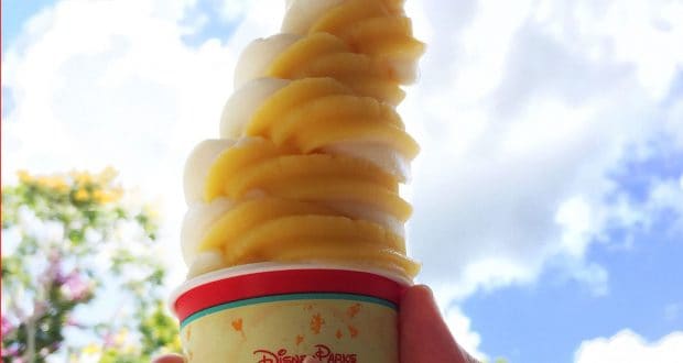 A refreshing Dole Whip swirl of pineapple and vanilla soft serve in a Disney Parks cup, held up to the magical blue sky.