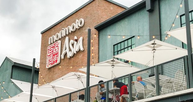 Outdoor seating at Morimoto Asia, shaded by white umbrellas, with the restaurant sign visible at Disney Springs in Walt Disney World.