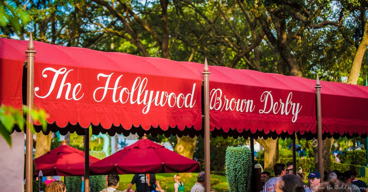 The iconic Hollywood Brown Derby red canopy at Disney’s Hollywood Studios, bustling with guests beneath lush trees.