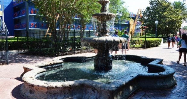 Charming stone fountain with flowing water in a lively plaza, surrounded by vibrant park attractions and festive entertainment.