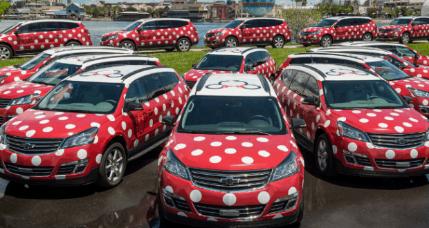 Minnie Vehicle Service cars, decked out with bows and polka dots, are parked by the waterfront at a Disney park.