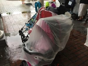 Strollers lined up on Disney World's rain-soaked bricks, each shielded by clear plastic covers during a sudden downpour.
