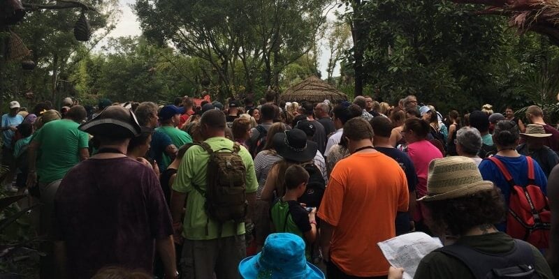 Guests form a long line outdoors at Walt Disney World, surrounded by lush greenery as they wait for their next magical adventure.