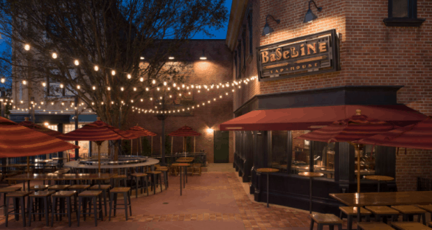 BaseLine Tap House outdoor patio at Disney World, glowing string lights, red umbrellas, and casual seating as evening sets in.