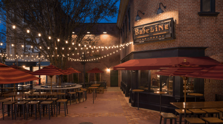 BaseLine Tap House outdoor patio at Disney World, glowing string lights, red umbrellas, and casual seating as evening sets in.