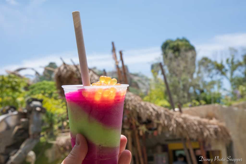 A vibrant boba drink with a straw is raised against the blue Florida sky at Walt Disney World, ready to fuel your park adventure.