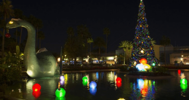 Christmas tree and Dino statue aglow with lights shimmer on the lake, channeling Disney World’s festive nighttime spectacle.