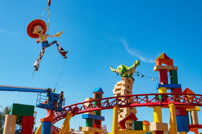 Jessie and Rex decorations soar above the Slinky Dog Dash coaster in Toy Story Land, all set against a vibrant blue sky.