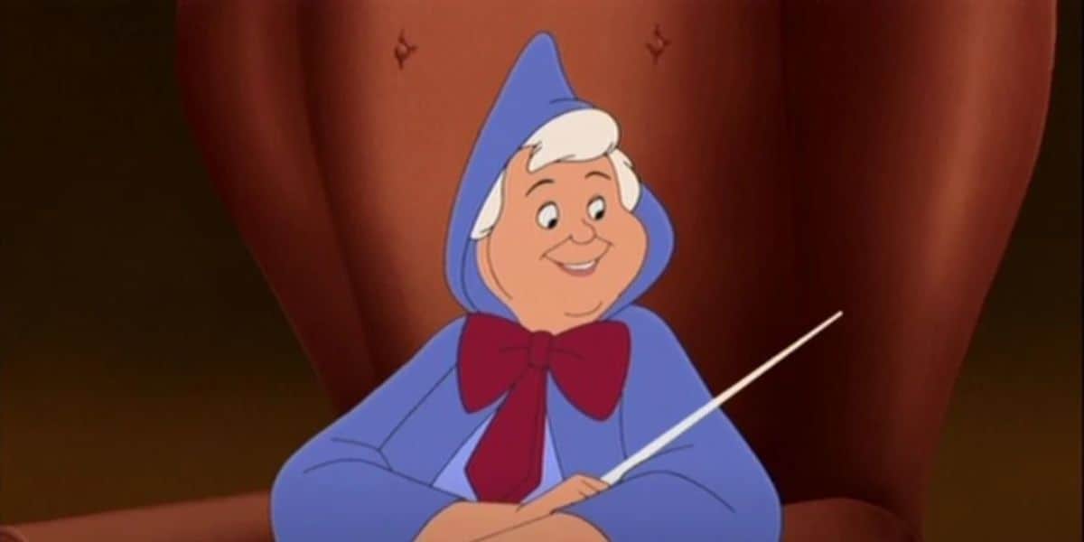 Animated character in a blue and red cloak, holding a wand, sitting on a large brown chair, smiling and looking to the side.