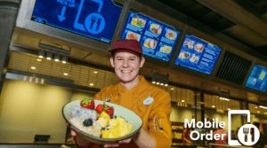 A friendly Cast Member presents fresh fruit, with digital menus and "Mobile Order" options at Walt Disney World dining locations.