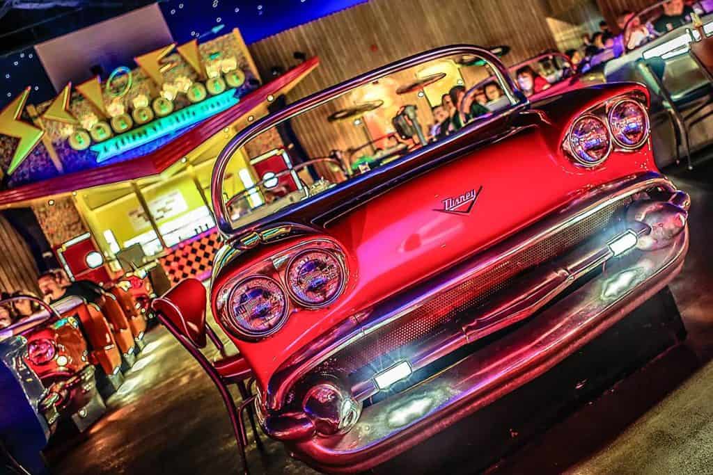 A classic red car booth at Sci-Fi Dine-In Theater in Disney World, with guests enjoying their meals under retro movie lights.