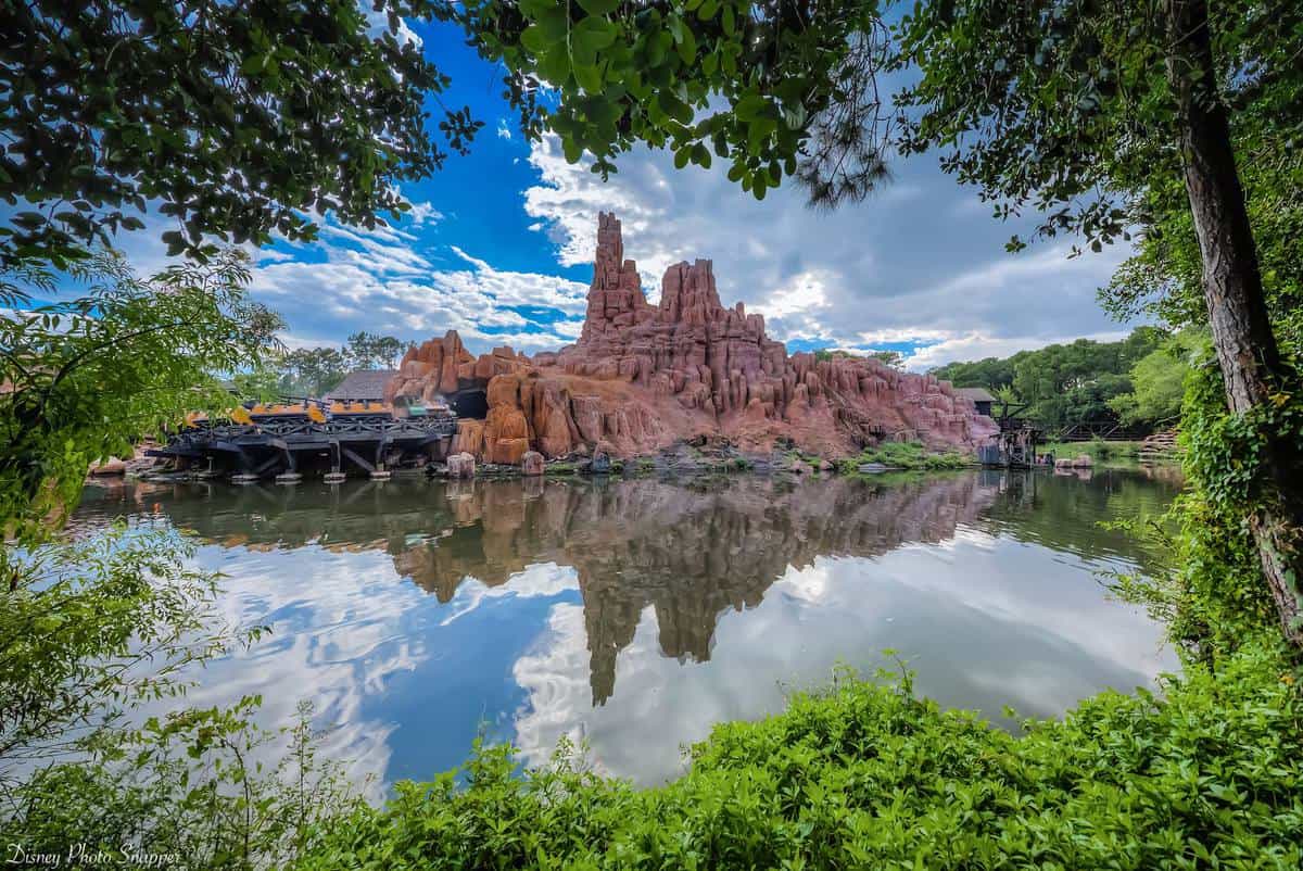 Iconic red rock mountain and serene lake, lush trees, and blue sky—evoking the magic of Frontierland at Walt Disney World.