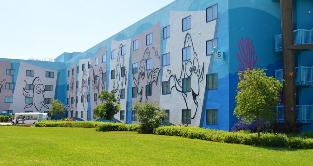 Blue Disney hotel with lively cartoon fish murals, lots of windows, and lush green grass—ideal for budget-savvy parkgoers.