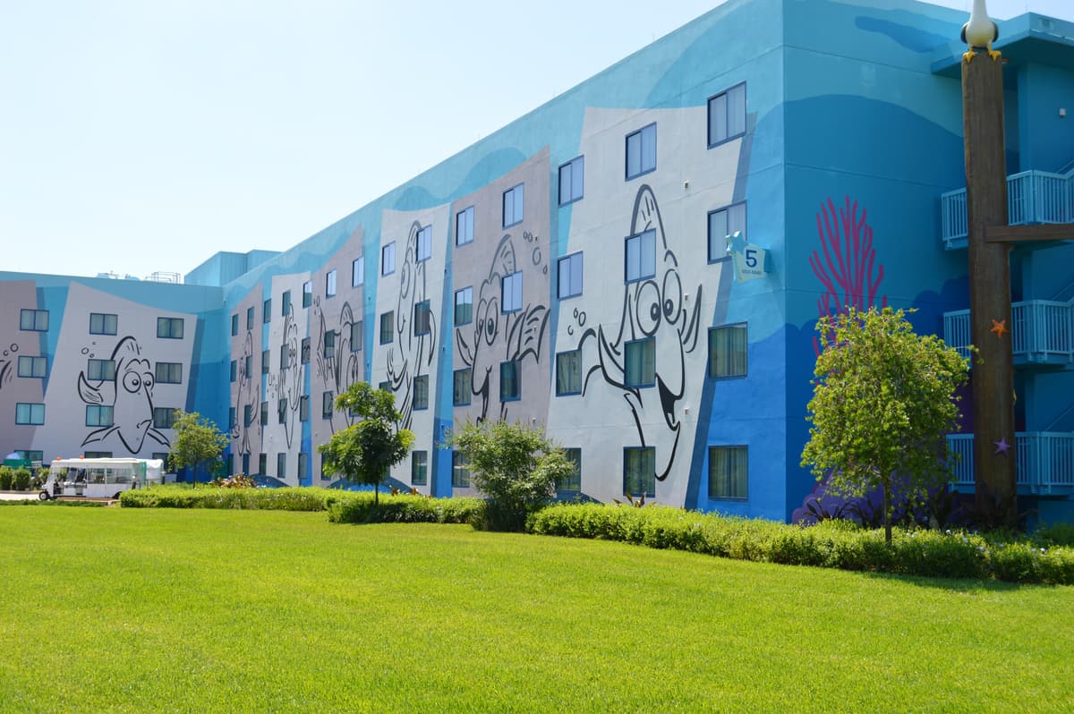 Blue Disney hotel with lively cartoon fish murals, lots of windows, and lush green grass—ideal for budget-savvy parkgoers.