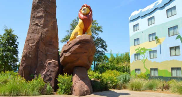 Majestic lion statue atop a rocky outcrop with lush landscaping and vibrant Disney resort in the background, ideal for trip planners.