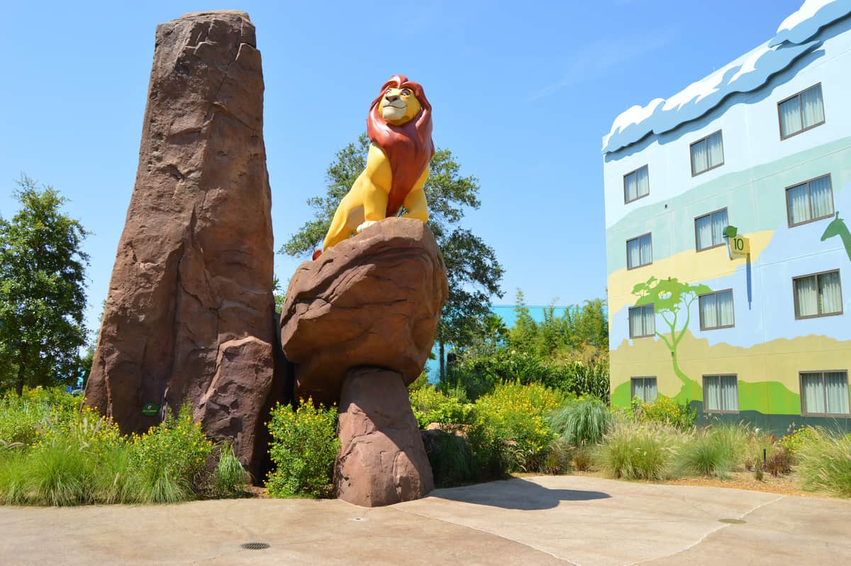 Majestic lion statue atop a rocky outcrop with lush landscaping and vibrant Disney resort in the background, ideal for trip planners.