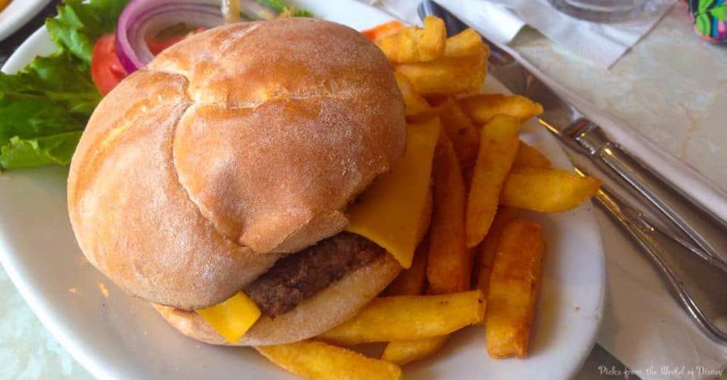 A classic Disney World cheeseburger with lettuce, tomato, and fries on a white plate—served with fork and knife for theme park magic.