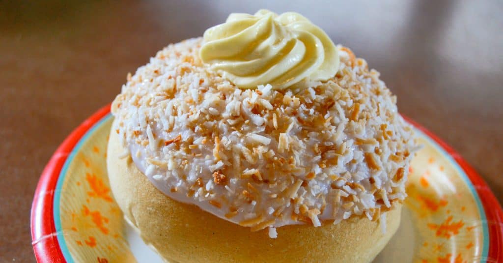 Sweet bun crowned with toasted coconut, icing, and a cream swirl—an iconic Disney World treat on a fun themed plate.