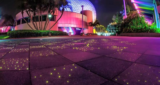 Spaceship Earth glows pink and purple at EPCOT, while palm trees and illuminated walkways create a stunning nighttime experience.