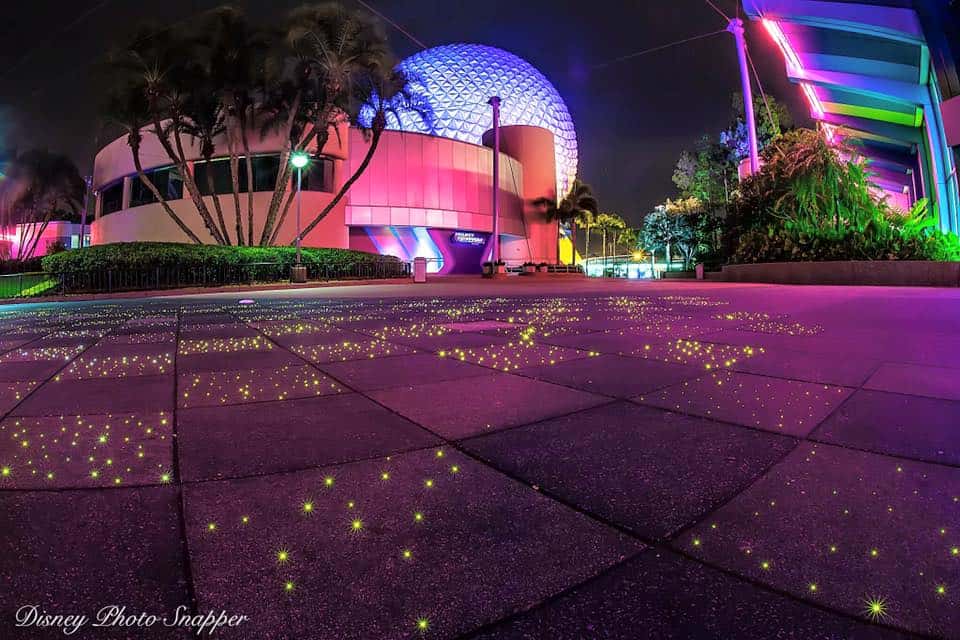 Spaceship Earth glows pink and purple at EPCOT, while palm trees and illuminated walkways create a stunning nighttime experience.