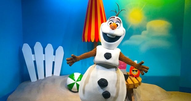 Olaf beams on a sunny Hollywood Studios beach, surrounded by a beach ball, umbrella, and painted sun at Disney World.