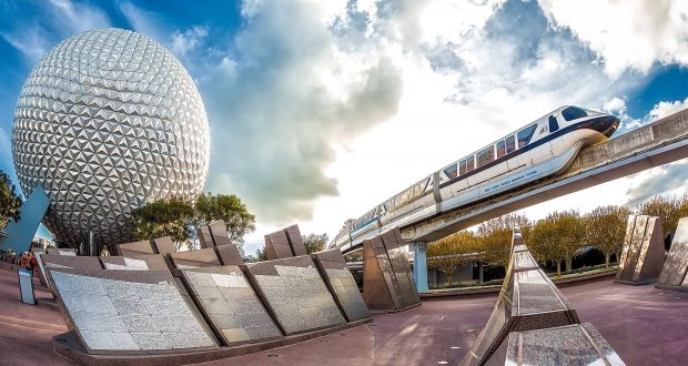 The Walt Disney World Monorail glides past Epcot’s iconic Spaceship Earth, set against a vibrant, partly cloudy Florida sky.