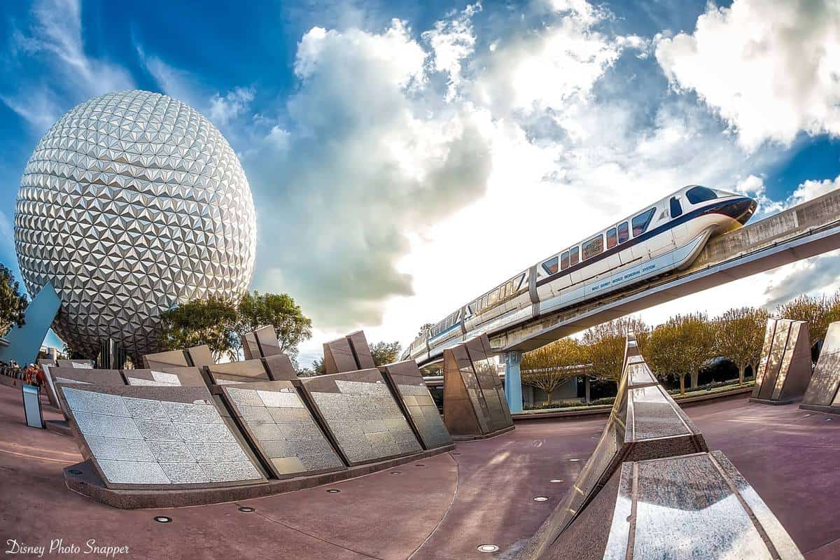 The Walt Disney World Monorail glides past Epcot’s iconic Spaceship Earth, set against a vibrant, partly cloudy Florida sky.