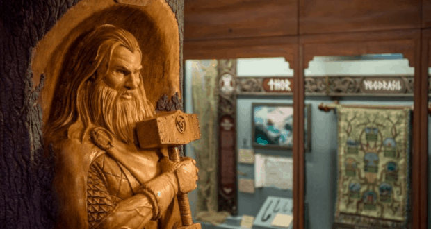 Thor statue, intricately carved in wood with his hammer, stands before an immersive Norse mythology display at the attraction.