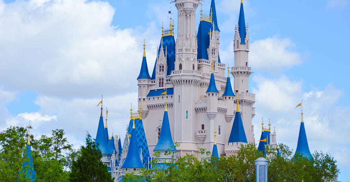 Cinderella Castle’s blue and white spires rise above lush trees under a clear sky—Walt Disney World’s iconic fairytale landmark.